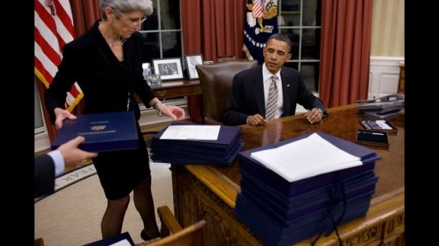With pen in hand, President Barack Obama sits at the Resolute Desk in the Oval Office as Staff Secretary Lisa Brown organizes a stack of 35 bills for him to sign into law, Jan. 4, 2011.